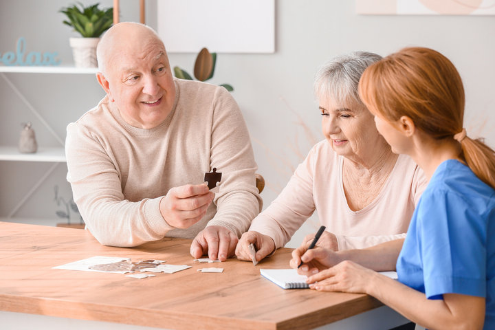 older man doing puzzle with resident and carer